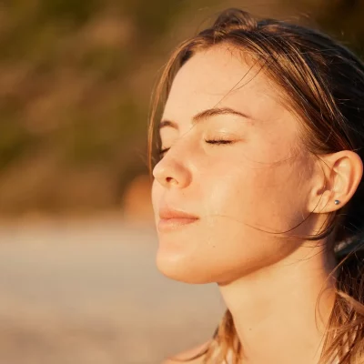 A woman sitting in the outdoors with her eyes closed as the sun hits her face.