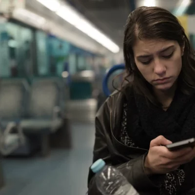 Young woman riding a bus at night is scrolling through social media on her phone looking depressed from what she sees.